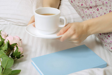 Beautiful young woman in bed drinking tea reading book