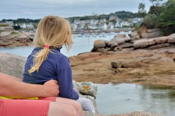 Une fillette assise sur les genoux de son père admire le paysage à Ploumanach en Bretagne