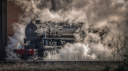 A steam train locomotive emerges from the mist, steam and smoke taken in a landscape side on view