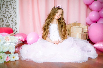 Girl with blond long hair in light-pink dress of a princess and tiara with balloons around