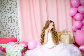 Girl with blond long hair in light-pink dress of a princess and tiara with balloons around