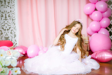 Girl with blond long hair in light-pink dress of a princess and tiara with balloons around