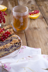 Homemade sweet pie for breakfast with lemon and berries of black currant and red currant. A glass of tea. Brown wooden background and free space for text or postcard.