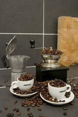 Still life of roast coffee beans, espresso cups and grinder on a tiled kitchen work surface