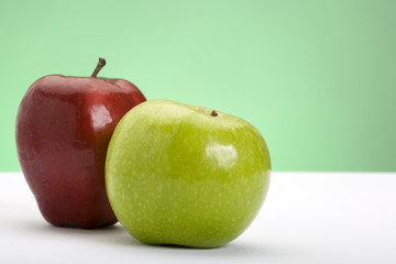 Two apples, one red, one green, on a white surface with green background