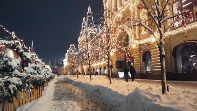 Beautiful Red Square New Year winter decorations, steady camera shot along night shining pedestrian street in the center of Moscow, trees with bright lights and balls are covered with snow.