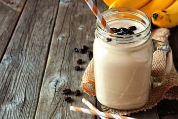 Coffee, banana smoothie in a mason jar. Side view with copy space over a rustic wood background.