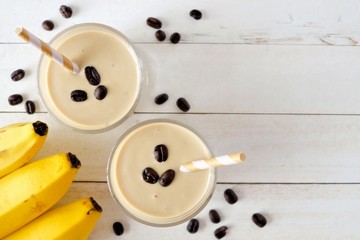 Coffee, banana smoothie in two glasses. Top view, corner orientation over a white wood background,