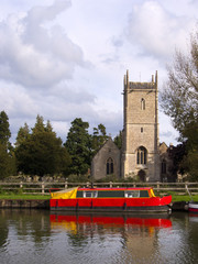 Colourful canal boats moored in early autumn sunshine near the church at Frampton-on-Severn on the Gloucester & Sharpness Canal, Gloucestershire, UK