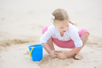 Cute little girl having fun on a sandy beach on warm and sunny summer day. Kid playing by the ocean.