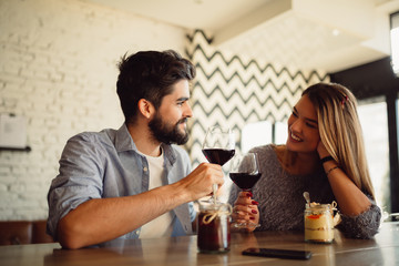 Couple clink glasses with red wine at date in casual outfit in cafe. Couple having romantic moments.