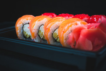 Beautiful rolls in the black container on black background with reflection, for a menu or website