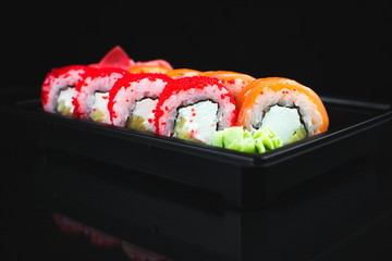 Beautiful rolls in the black container on black background with reflection, for a menu or website