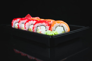 Beautiful rolls in the black container on black background with reflection, for a menu or website