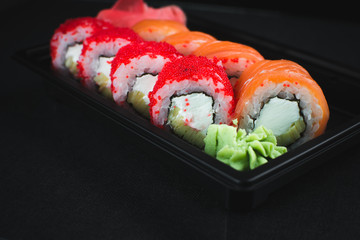 Beautiful rolls in the black container on black background with reflection, for a menu or website