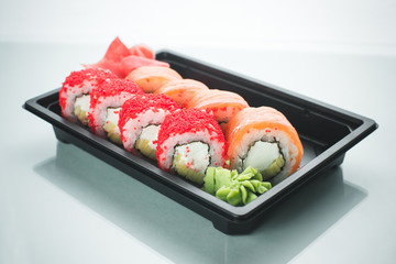 Beautiful rolls in black container on white background with reflection, for a menu or website