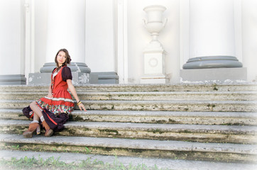 young beautiful brunette in boho style costume sits on the steps of the Palace