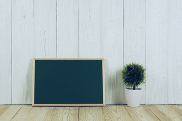 Blank green chalkborad with wood frame and little decorative tree in white vase on wooden table...