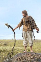 rustic man in a burlap shirt stands on a stone leaning on a wooden stick