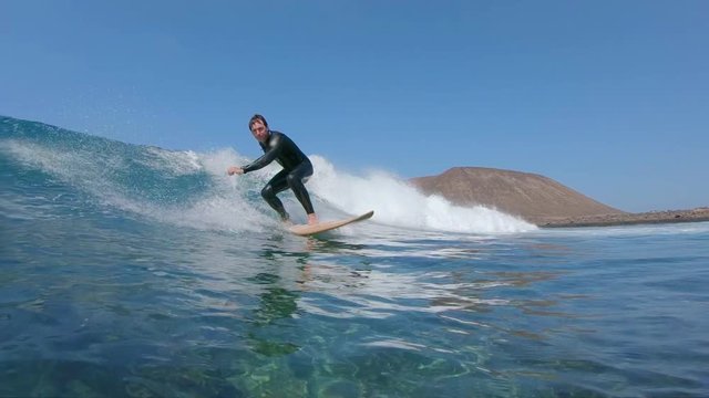 SLOW MOTION UNDERWATER: Fit surfer dude on vacation surfing ocean wave. Surfer riding awesome big wave near volcanic island. Cinematic shot of male on surfboard before dipping into crystal clear water