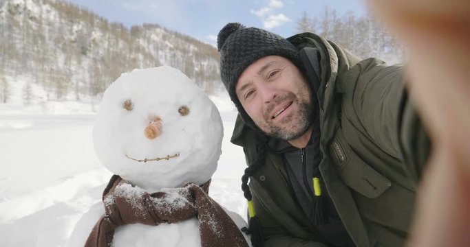 On a winter day, a man in the mountains makes a video call and greets his wife or friends on the phone. Concept of: winter holidays, technology, christmas, connection
