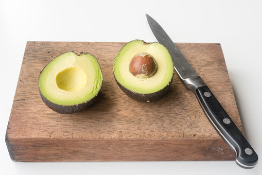 Low angle view of avocado cut in half on chopping board with knife (selective focus)