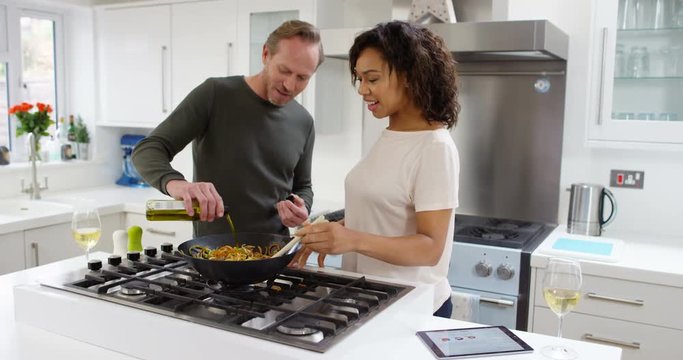 4K Happy couple cooking at home, following a recipe on computer & drinking wine. Slow motion.