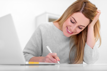 Attractive young woman in a good mood works with documents in the office or at home. Writes, fills papers at the desk with a laptop.