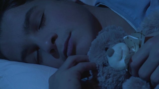 Sweet healthy dream of school boy cuddling teddy bear, comfortable mattress