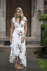 Stunning young blonde woman in white floral print dress poses for portraits in front of mansion home - fashion