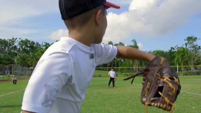 Slow motion from behind of kid as he throws ball during baseball practice