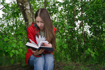 dark-haired student in a red jacket sitting in the Park near delleva and reading a book