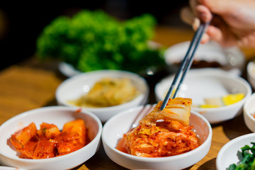 Woman hand holding chopsticks for eating Kimchi salad in restaurant. Korean food traditional Kimchi