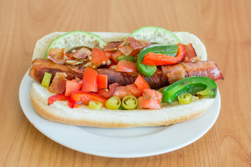 Los Angeles style hot dog with bacon wrapped sausage, mayonnaise, sauteed onions and peppers, tomato with cilantro, hot pepper, avocado and bacon bits.