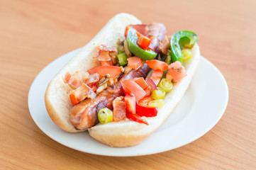Bacon-Wrapped Hot Dog with bacon wrapped sausage, mayonnaise, sauteed onions and peppers, tomato with cilantro, hot pepper and bacon bits.