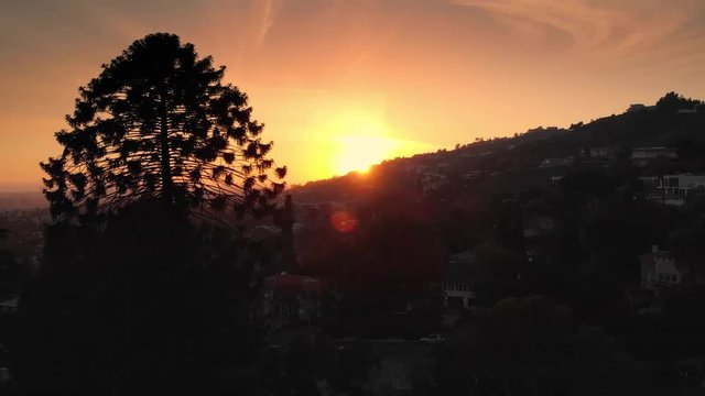 Aerial view of sunset sun peaking over Hollywood Hills skyline, Los Angeles cityscape in background. 4K UHD.