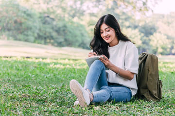 Woman with pen writing on a notebook sitting on grass in park