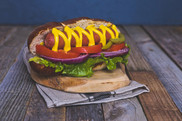 Delicious hot dog with toppings on dark wooden background.