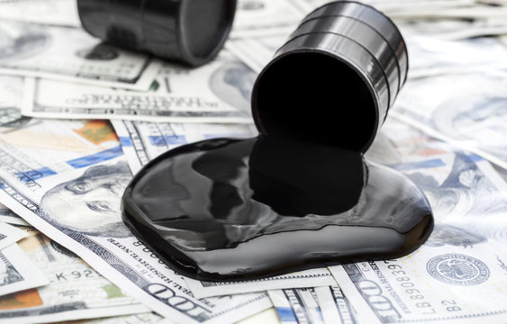Whole barrel of oil and crude oil spilled from barrel on the dollar bills.