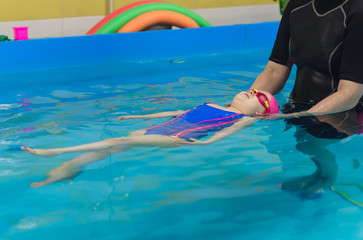 A little girl of European appearance in a pink rubber cap learning to swim in the pool