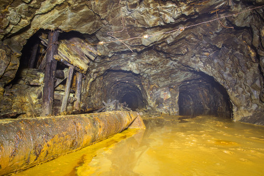 Underground abandoned gold ore mine shaft tunnel gallery with yellow water sulfur flooded
