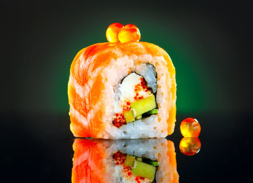 Sushi roll over black background. California sushi roll with salmon, vegetables, flying fish roe closeup. Japanese food 