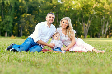 Happy family in a park in summer autumn. Mother, father and baby play in nature in the rays of sunset.