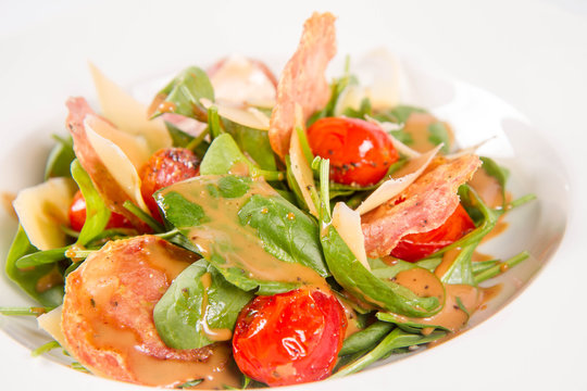 Baby spinach, dry sausage, matured cheese, roast tomatoes, thyme-balsamic vinaigrette salad on a white background