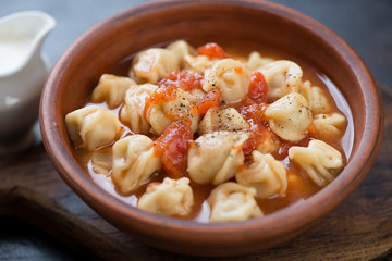 Soup with meat dumplings pelmeni served in a clay bowl, selective focus, closeup
