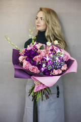 The beautiful rustic bouquet in purple tones in woman hands on grey background