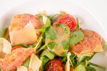 Baby spinach, dry sausage, matured cheese, roast tomatoes, thyme-balsamic vinaigrette salad on a white background