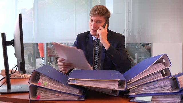 Angry shouting on cell phone executive business man with pile of documents files