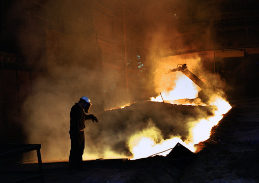 Man on blast furnace casting stage with hot molten iron in sand runners.