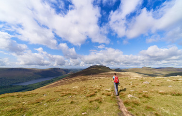 A female hiker walking a narrow trail towards the summit of Great Borne with Ennerdale Water to the...